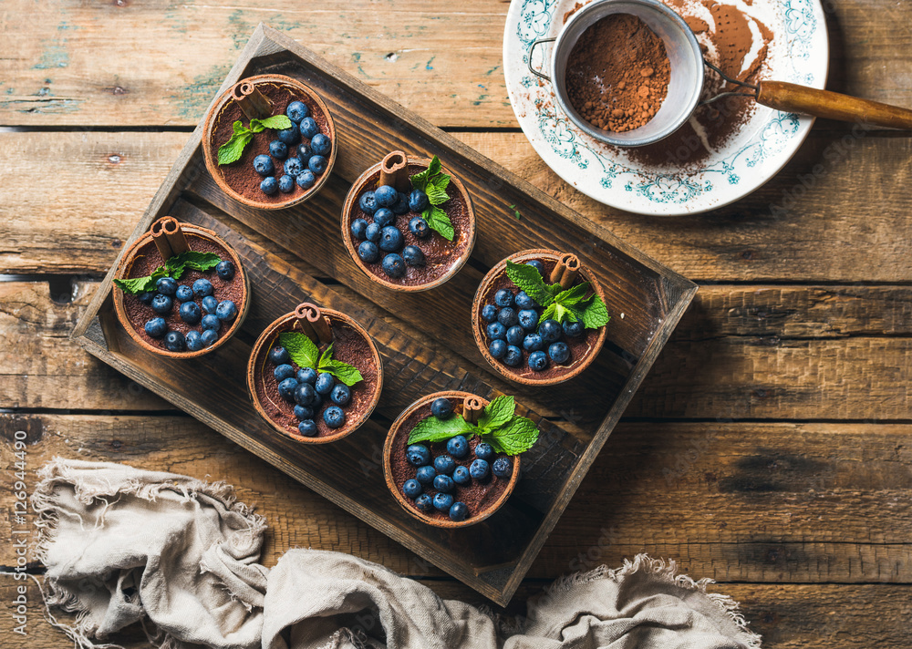 自制提拉米苏甜点，装在玻璃杯里，肉桂、薄荷和新鲜蓝莓放在木托盘里，还有si