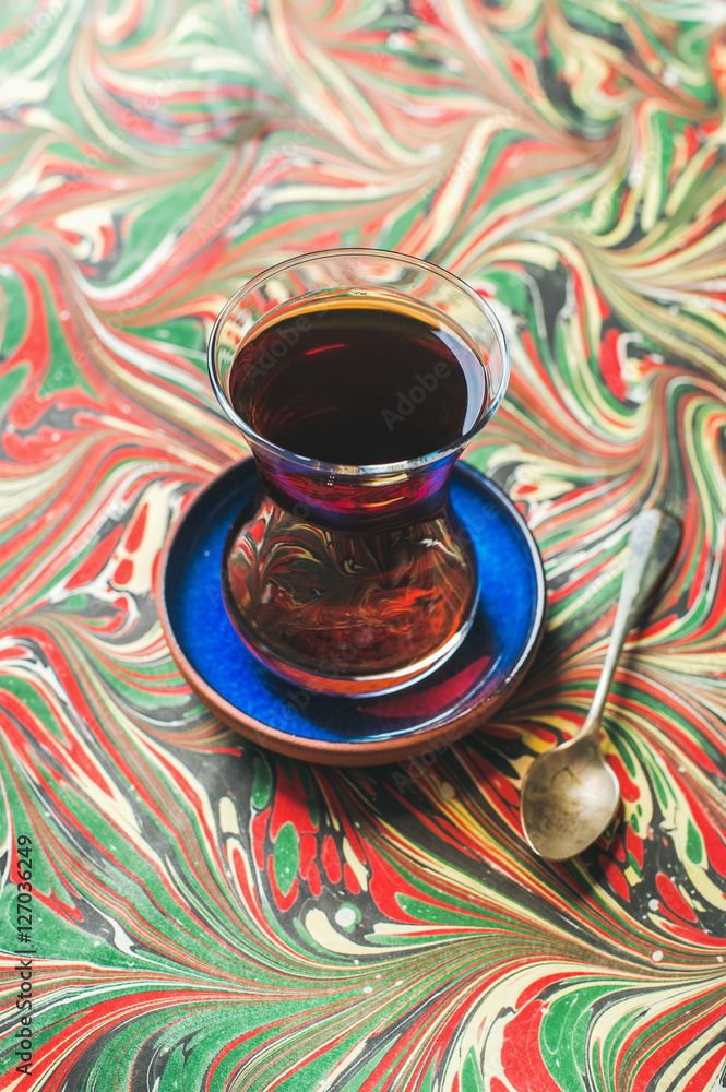 土耳其茶，用传统的东方郁金香玻璃杯和勺子舀在ebru彩绘的彩色纸背景上