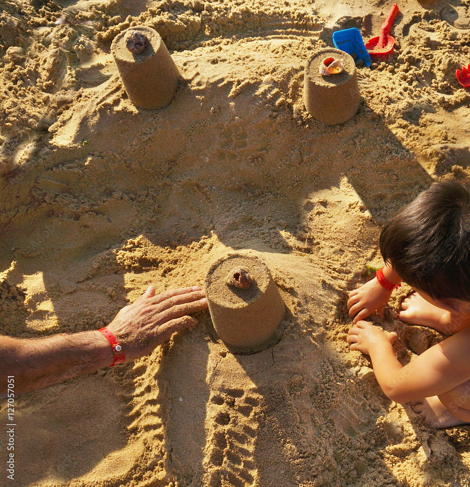 爸爸和儿子在海滩上用沙子建造塔楼，在度假胜地的海上避暑