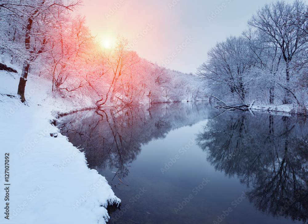 Winter forest on the river at sunset. Colorful landscape with snowy trees, beautiful frozen river wi