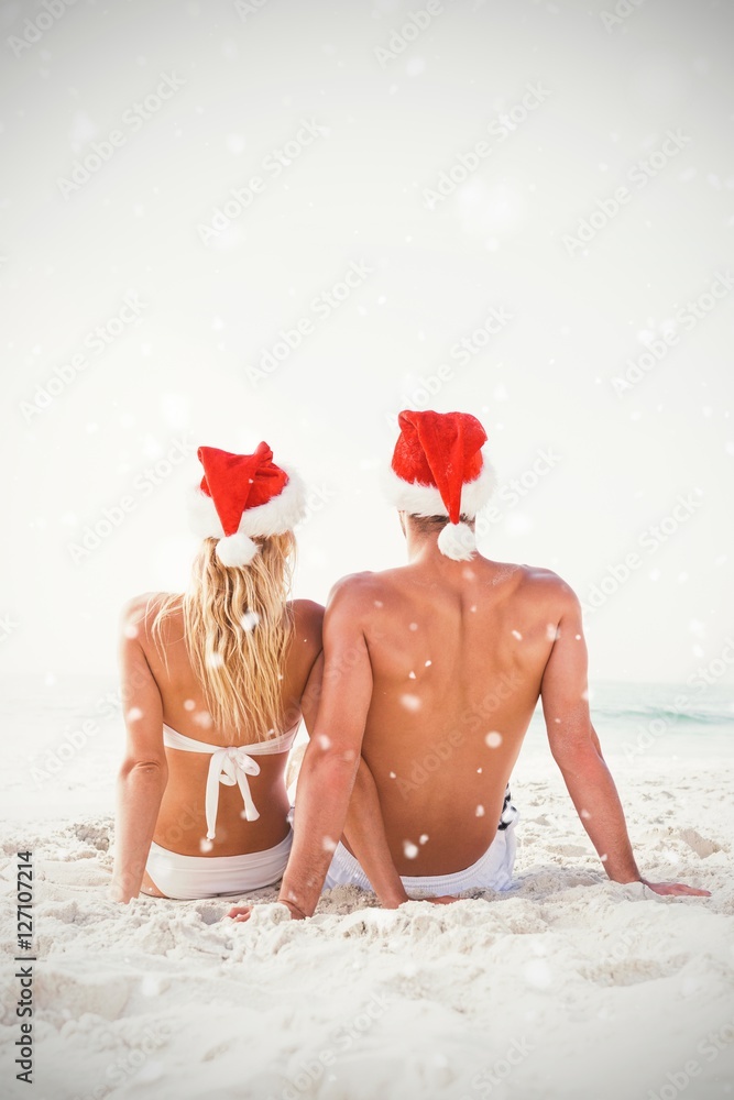 Composite image of couple wearing santa hat at beach