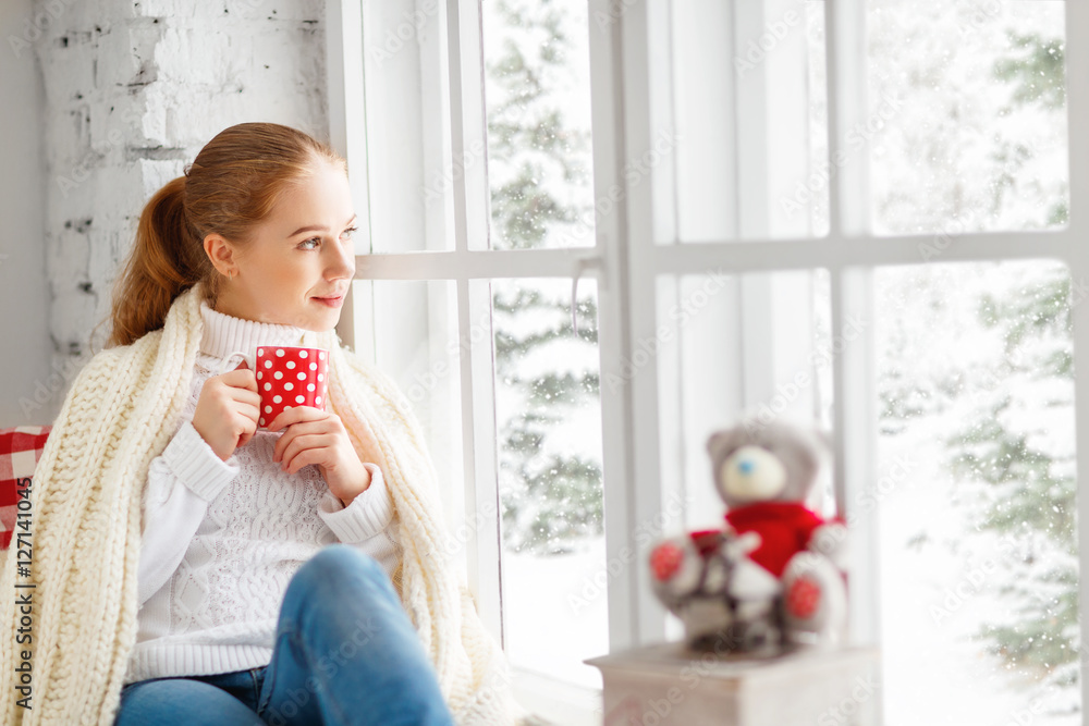 快乐的年轻女人，在冬窗圣诞节喝杯热茶