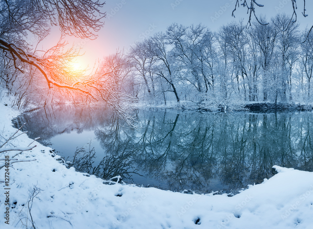 日落时河边的冬季森林。白雪皑皑的树木、阳光、美丽的冰冻ri的全景景观