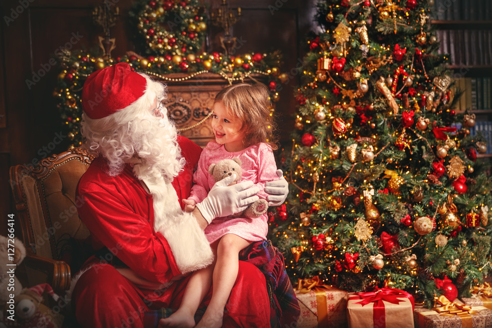 穿着睡衣的小女孩坐在圣诞老人的腿上围着圣诞老人