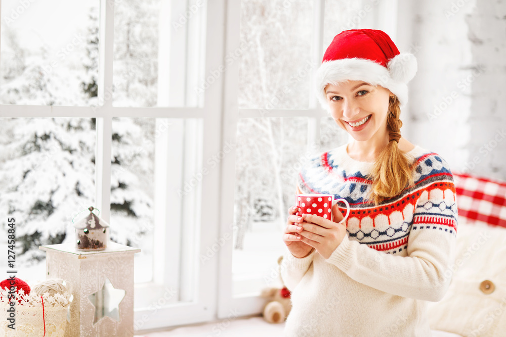 快乐的年轻女人，在冬窗圣诞节喝杯热茶