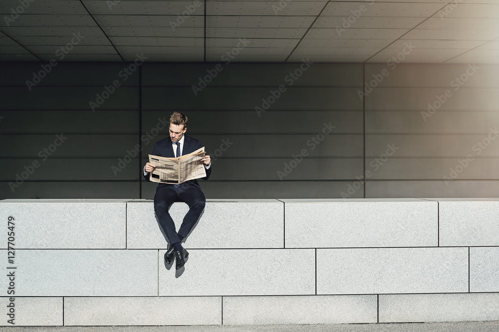 坐在砖墙上看报纸的商人