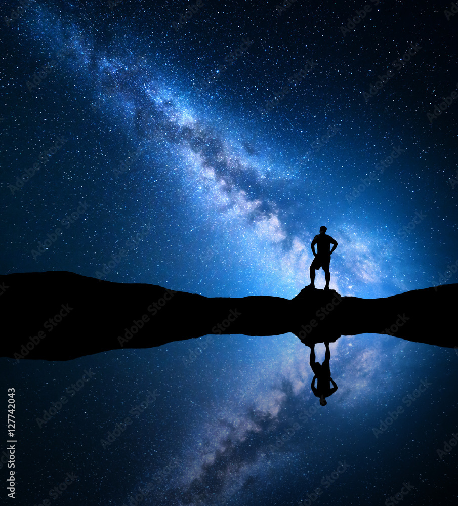 银河系。有星星的夜空和湖边山上一个孤独的人的剪影