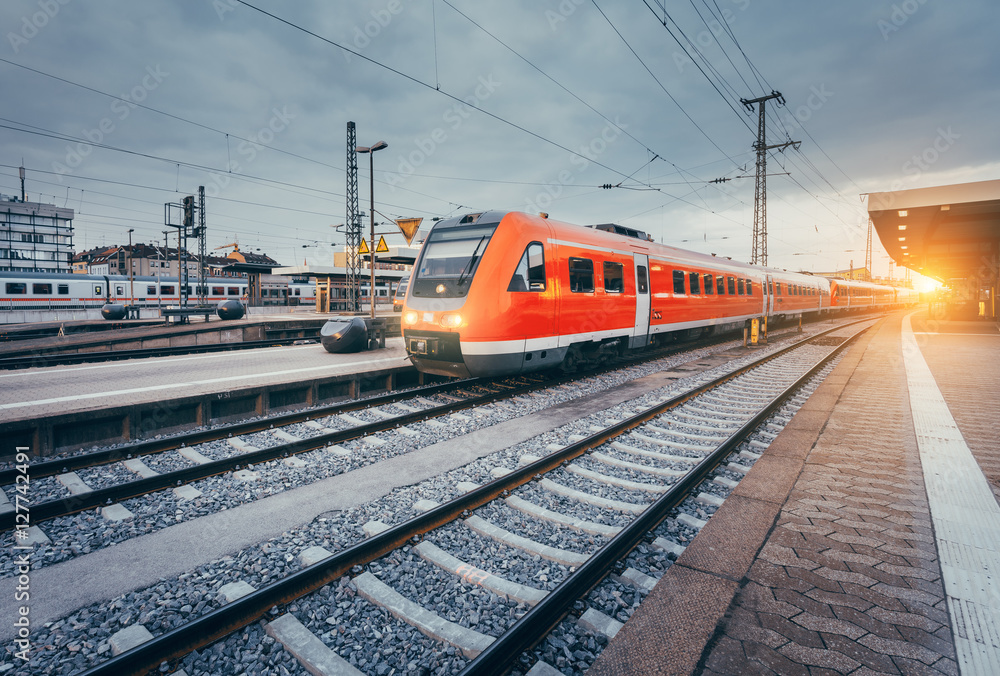 彩色日落下火车站的现代高速红色通勤列车。带葡萄酒标签的铁路