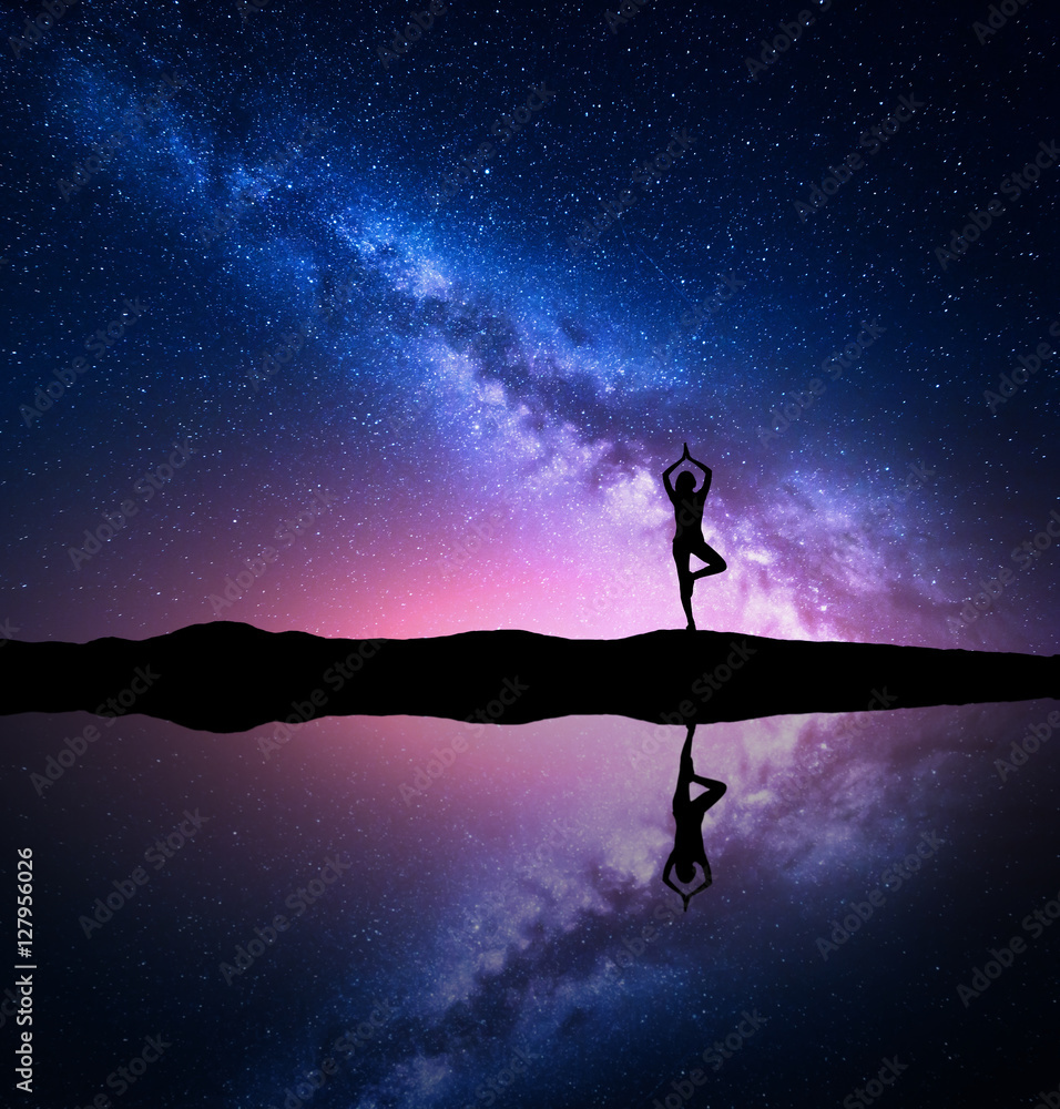银河系。一个站着的女人在池塘附近的山上练习瑜伽的剪影，天空参考