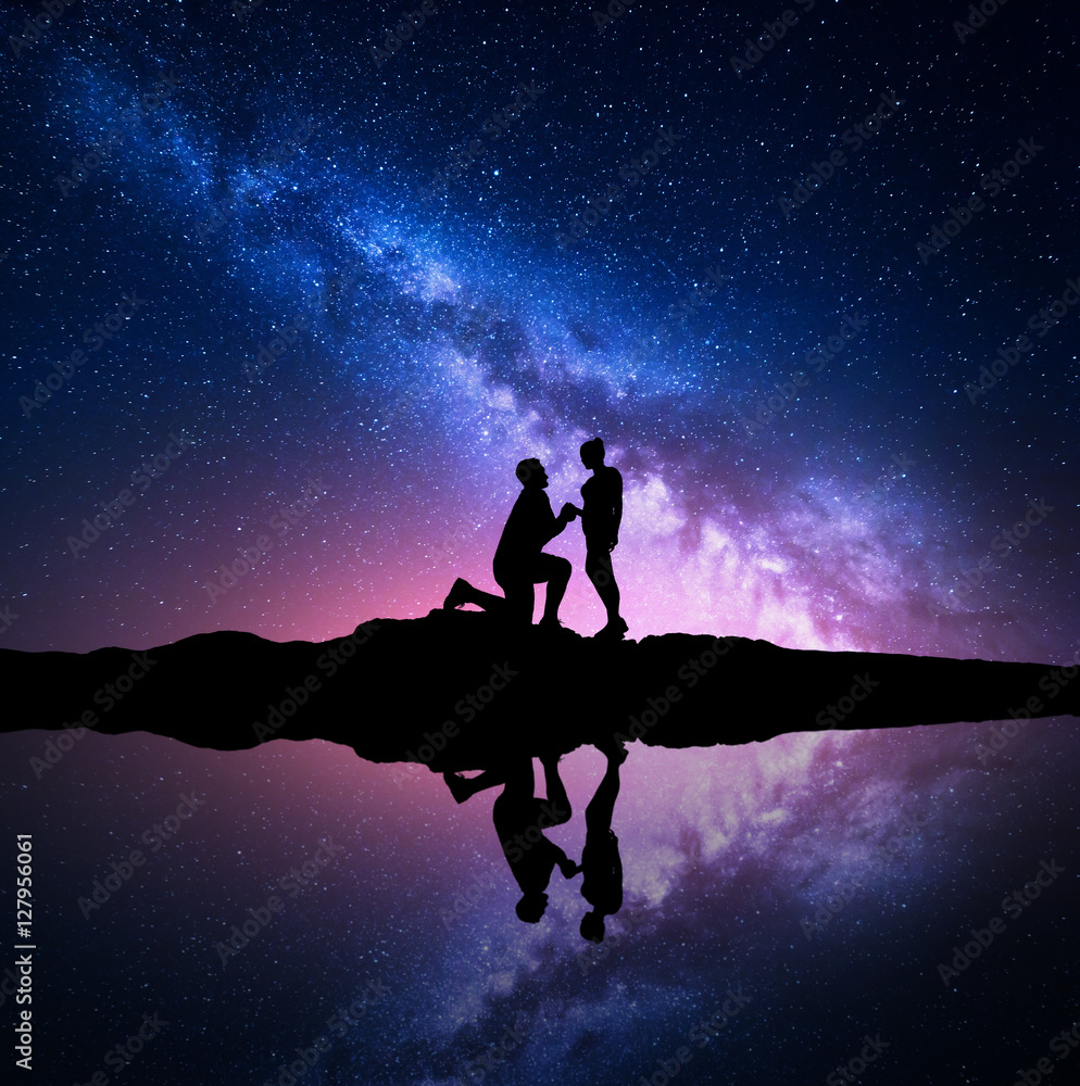 银河系。一名男子在湖边的小山上向女友求婚的剪影