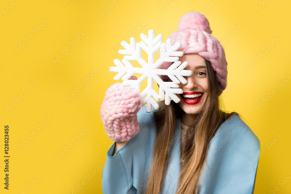 Happy woman in colorful winter clothes holding a beautiful snowflake standing on the yellow backgrou