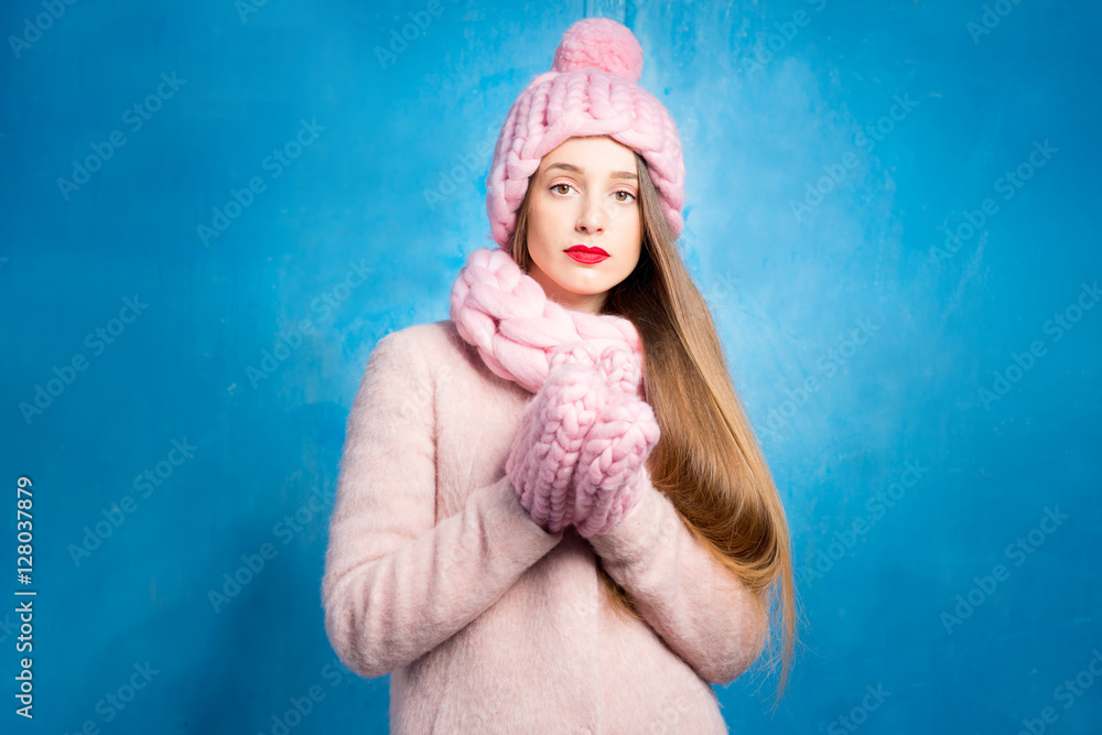 蓝色背景下，一个穿着针织粉色皮屑、手套和帽子的悲伤女人的冬季肖像