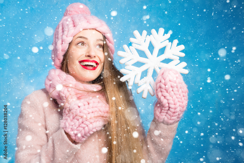 一位穿着针织粉色皮屑、手套和帽子的美女的冬季肖像，帽子上有雪花