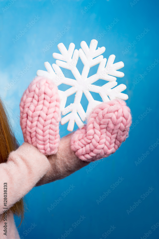 手戴针织手套，蓝色背景下有一片美丽的大雪花