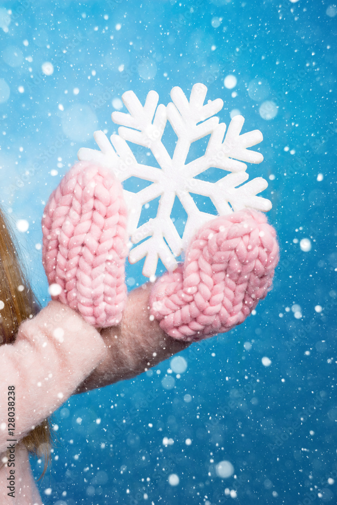 手戴针织手套，蓝色背景下有一片美丽的大雪花