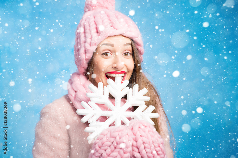 Winter portrait of a beautiful woman in knitted pink scurf, gloves and hat with snow flake on the bl