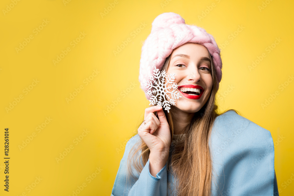 快乐的女人，穿着五颜六色的冬装，手里拿着一朵美丽的雪花，站在黄色的背上