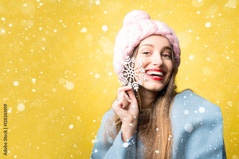 快乐的女人，穿着五颜六色的冬装，手里拿着一朵美丽的雪花，站在黄色的背上