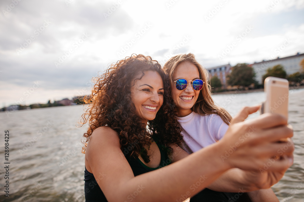 Female friends taking selfie with mobile phone by the lake