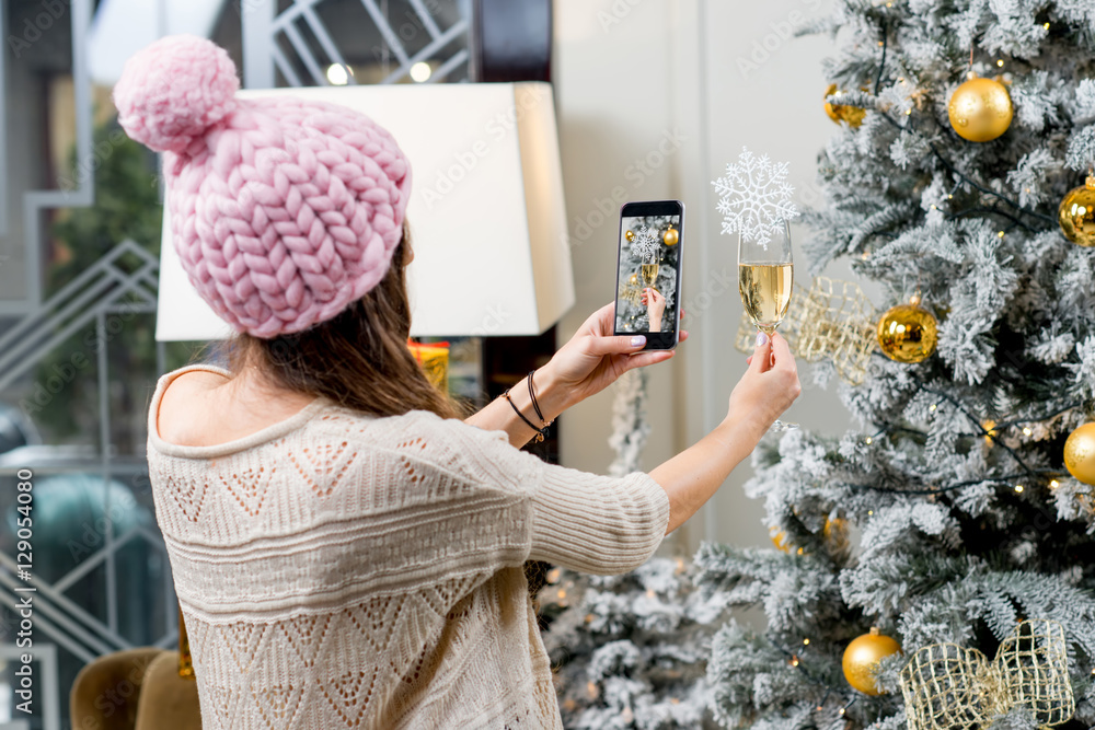 一名女子用智能手机在圣诞树背景上拍摄一杯起泡酒