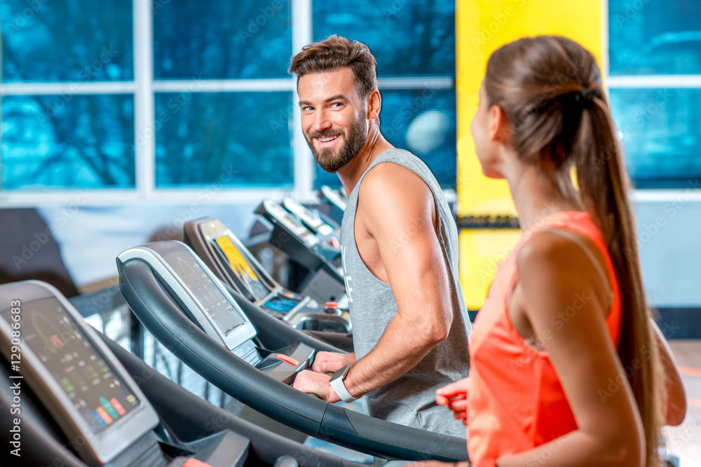 年轻的运动情侣在健身房的固定跑步机上进行有氧运动。