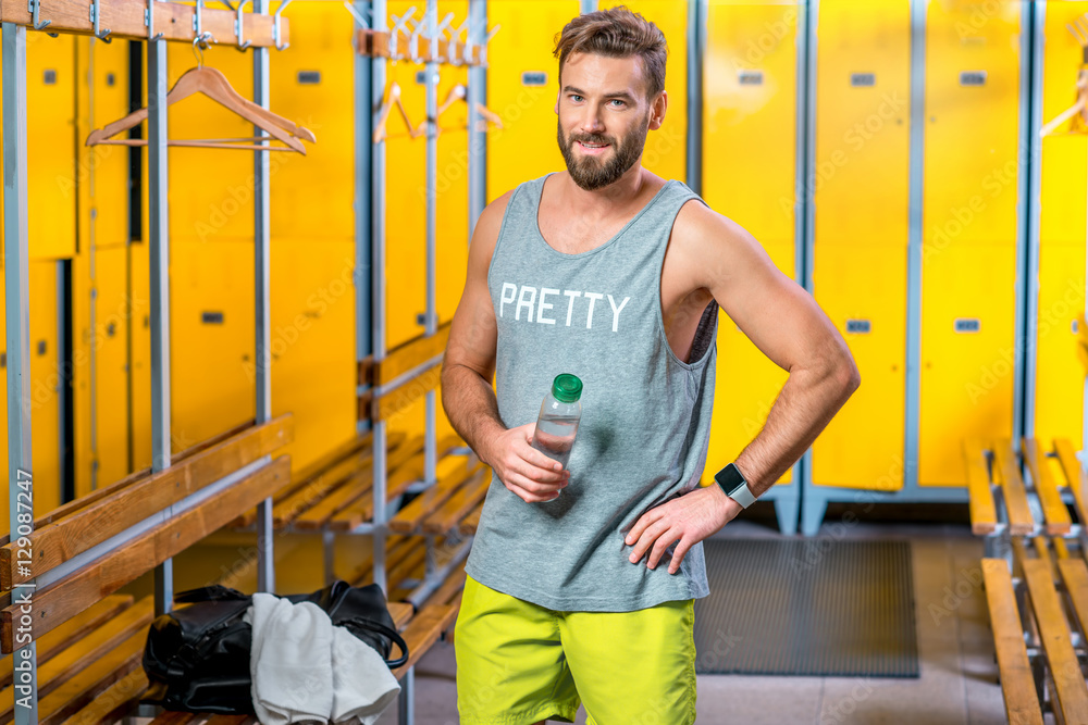 运动员拿着一瓶水站在健身房的更衣室里。赛后喝水