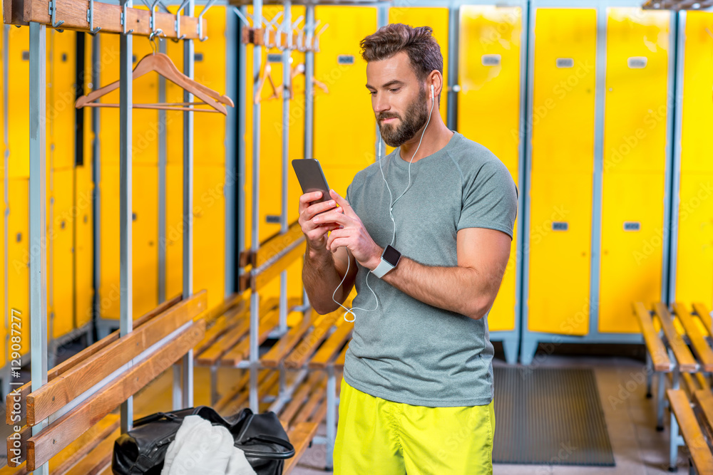 帅气运动男在健身房更衣室用智能手机听音乐