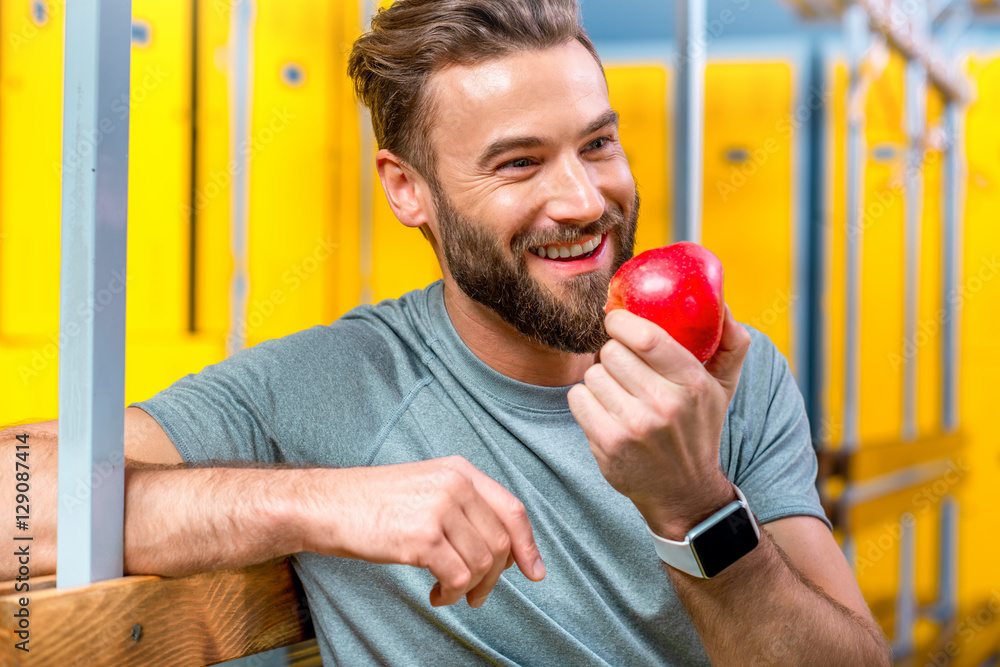 运动男训练结束后坐在健身房更衣室吃苹果。健康自然
