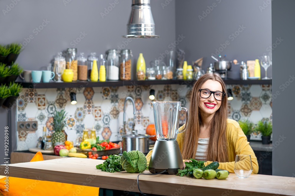 年轻女子坐在桌子上，家里有新鲜的绿色蔬菜和搅拌机的肖像
