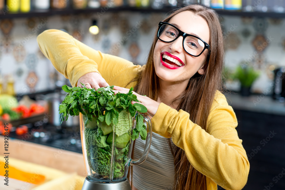 年轻微笑的女人在家里的厨房里把新鲜的绿色蔬菜推入搅拌机。健康的素食主义者