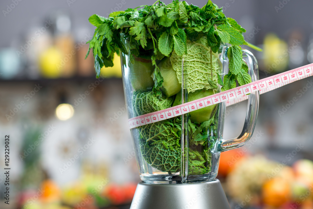 装满绿色水果和蔬菜的搅拌机的特写，准备与厨房里的计量器混合