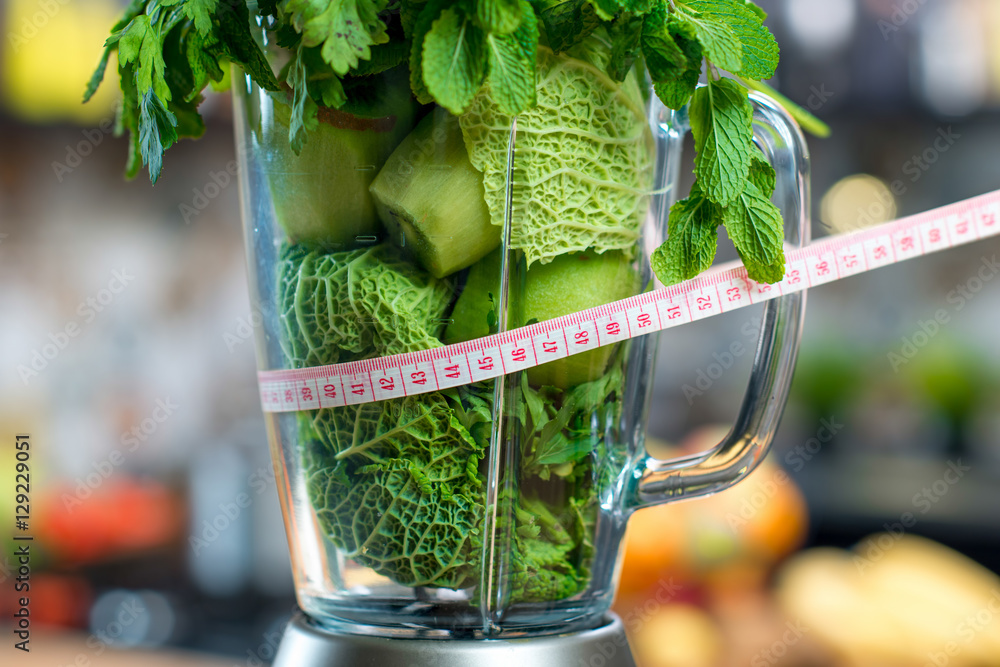 装满绿色水果和蔬菜的搅拌机的特写，准备与厨房里的计量器混合