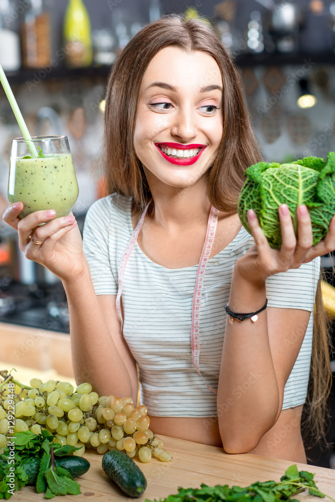 家里厨房里年轻微笑的女人拿着绿色奶昔的画像。健康素食