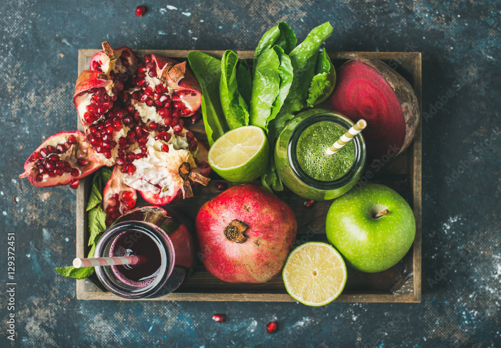 Green and purple fresh juices or smoothies with fruit, greens, vegetables in wooden tray, top view, 