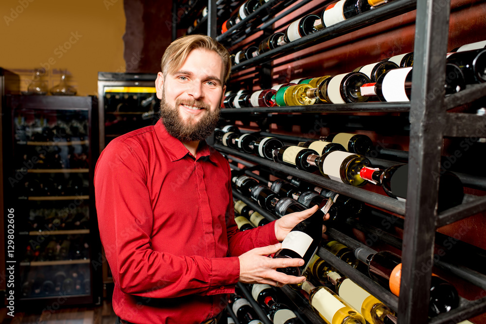 一位英俊的侍酒师的画像，他在豪华酒店的货架前拿着一杯葡萄酒和瓶子