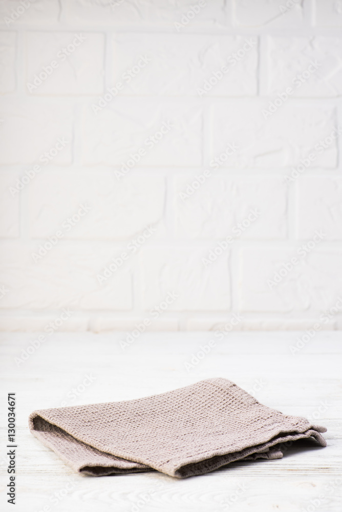 Gray napkin isolated on white wooden table. Copy space. Brick wall background. Front view.