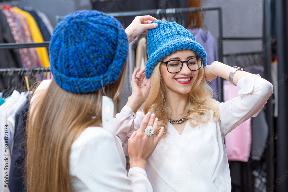 Two beautiful women trying blue hats in the clothing store. Happy winter shopping
