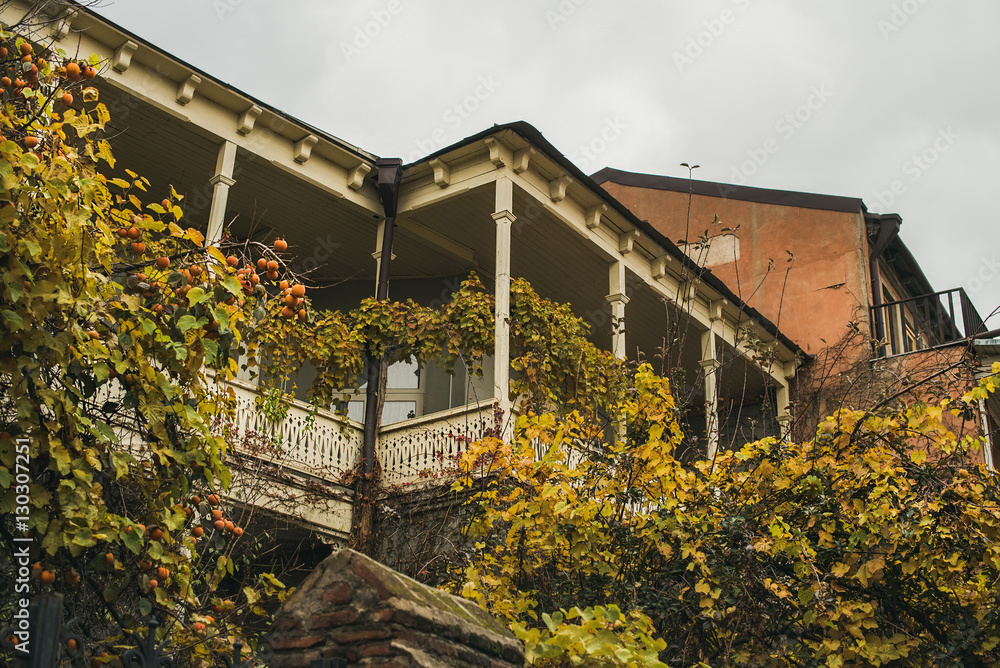 Typical house exterior of Tbilisi old town center in Autumn. Shabby house with wooden balcony, fruit