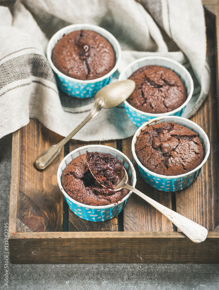 Chocolate souffle in blue individual baking cups in wooden serving tray over grey concrete backgroun