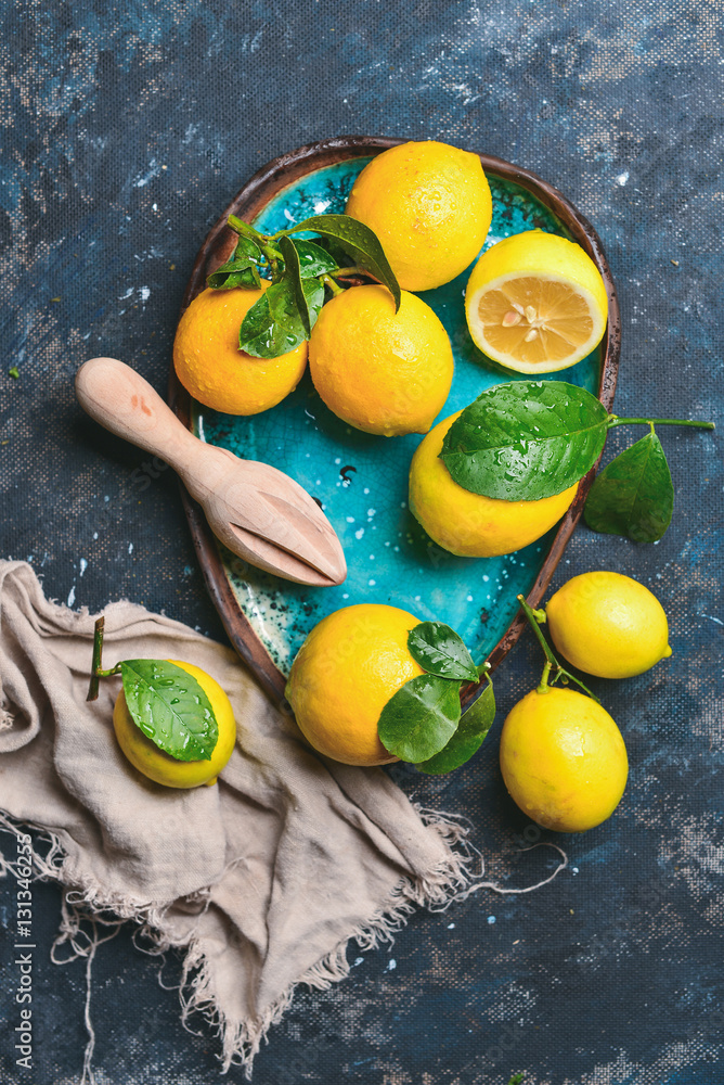 Freshly picked lemons with leaves in blue ceramic plate over dark blue shabby plywood background, to