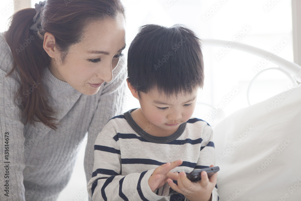 Mother and child are watching smartphone together in the bedroom