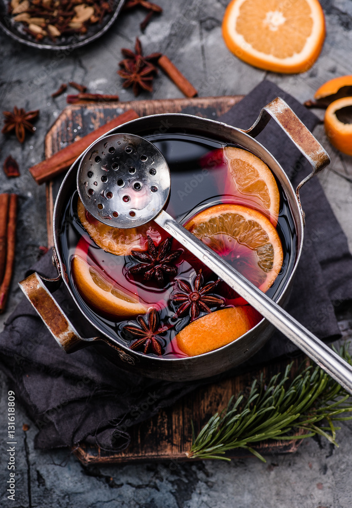 Mulled wine with orange, spices and strainer in aluminum vintage casserole on wooden board. Concrete