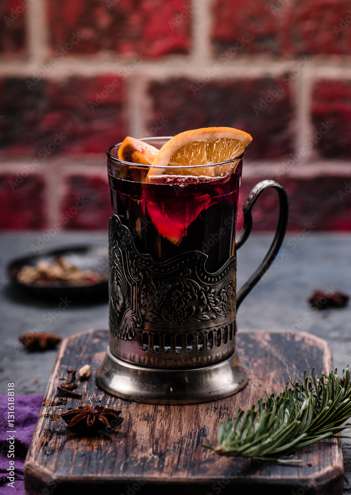 Mulled wine with orange and spices in vintage glass cup holder on wooden board. Concrete background.