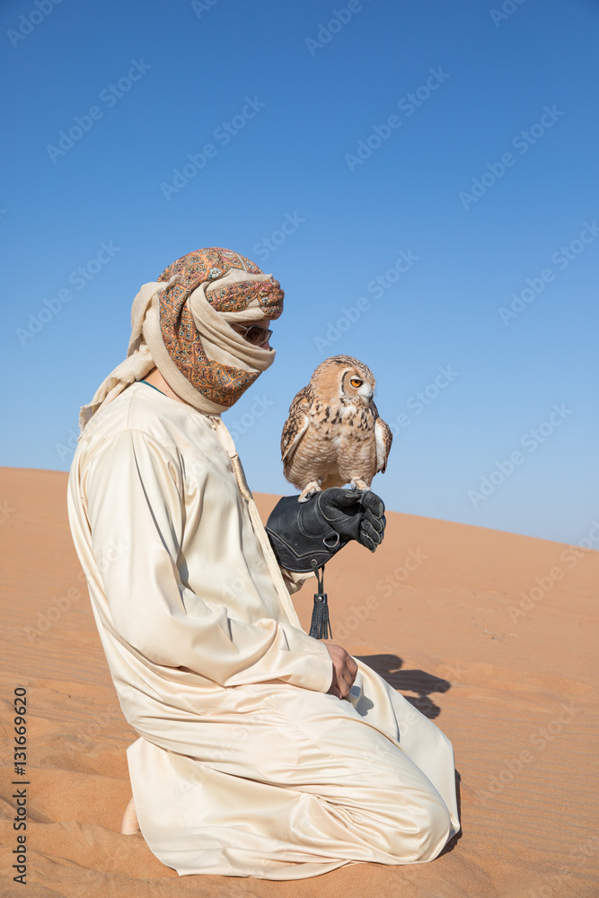 Young male pharaoh eagle owl (bubo ascalaphus) with a traditionally dressed arab male during a deser