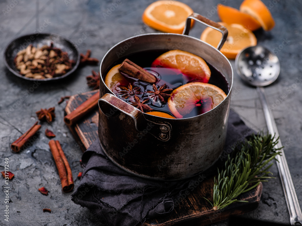 Mulled wine with orange, spices and strainer in aluminum vintage casserole on wooden board. Concrete