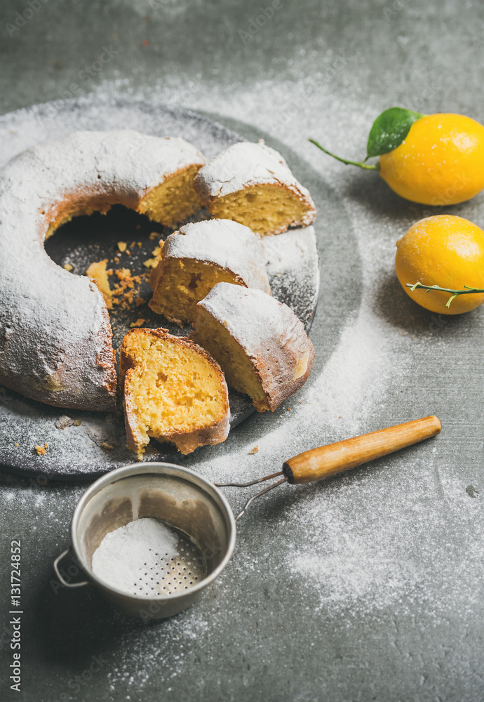 Homemade gluten-free lemon bundt cake with sugar powder over grey concrete background, selective foc