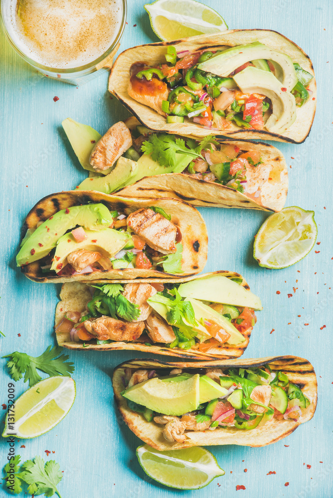 Healthy corn tortillas with grilled chicken, avocado, fresh salsa, limes and beer in glass over blue