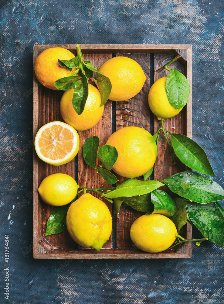 Freshly picked lemons with leaves in rustic wooden tray over dark blue shabby plywood background, to