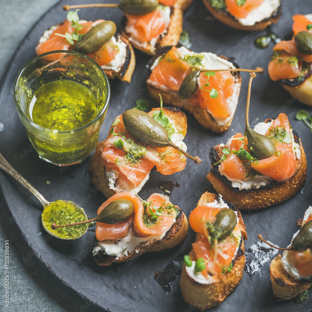 Homemade salmon crostini with cream-cheese, watercress, capers and pesto suace in round black slate 