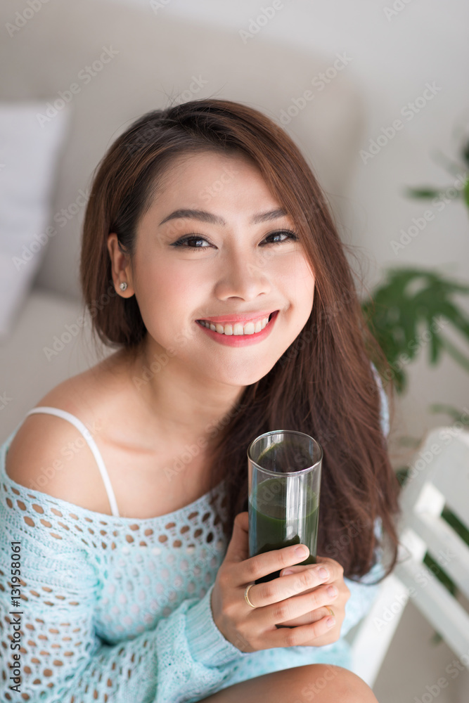 Smiling young asian woman drinking green fresh vegetable juice o